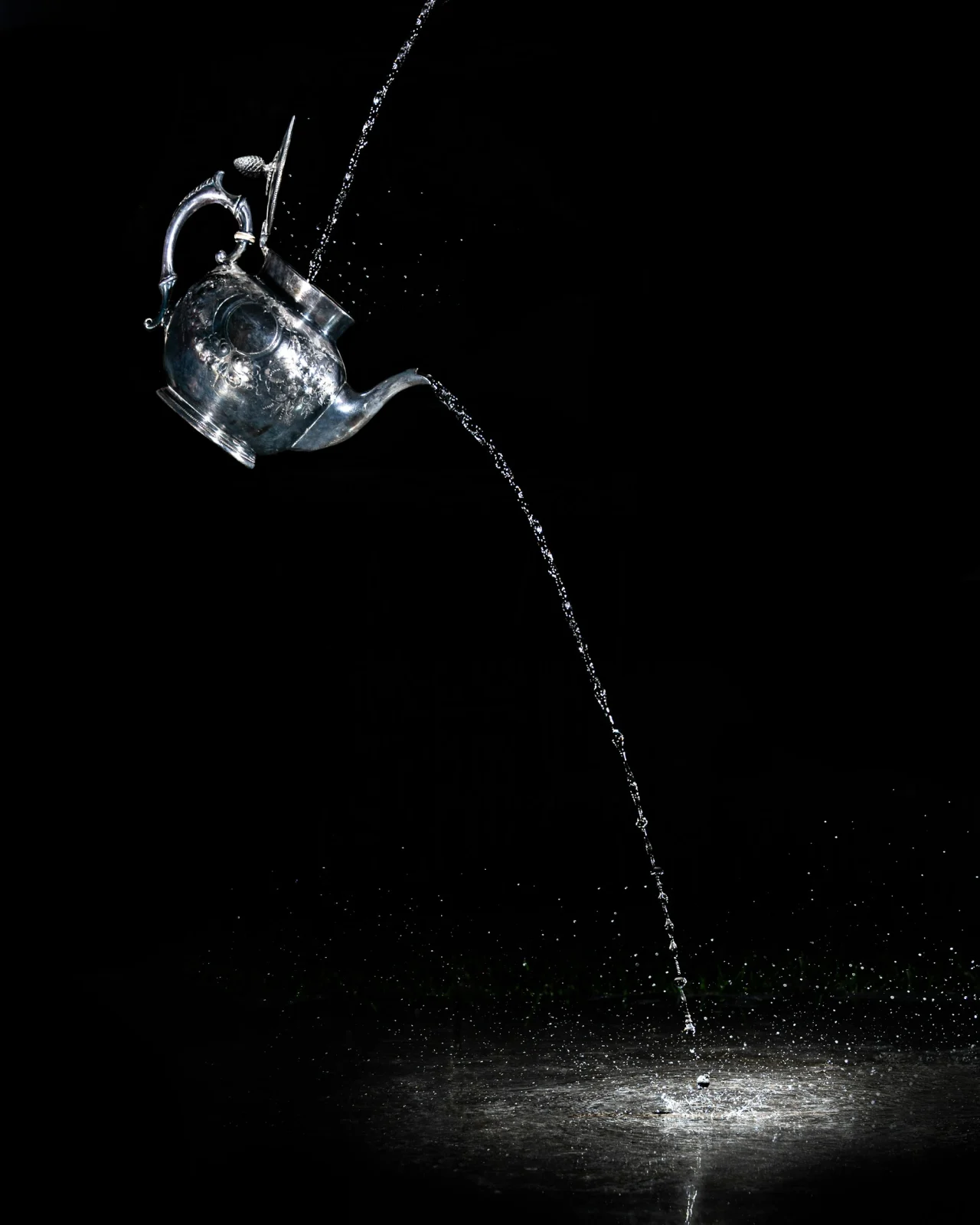 Water pouring from a glass kettle on black
